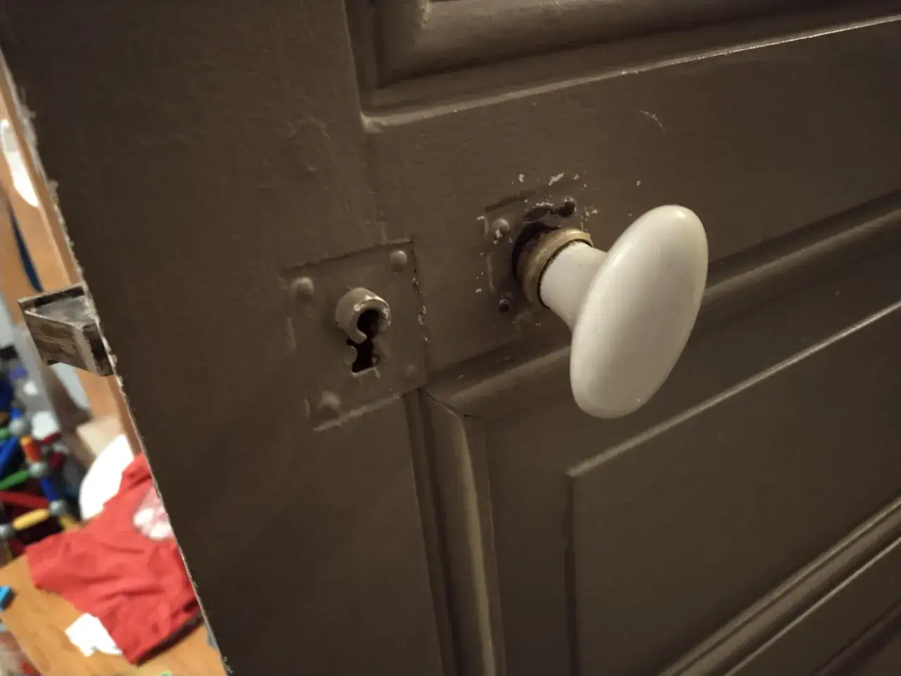 Gros plan sur le mécanisme poignée porte ancienne, avec une poignée blanche et une serrure visible.