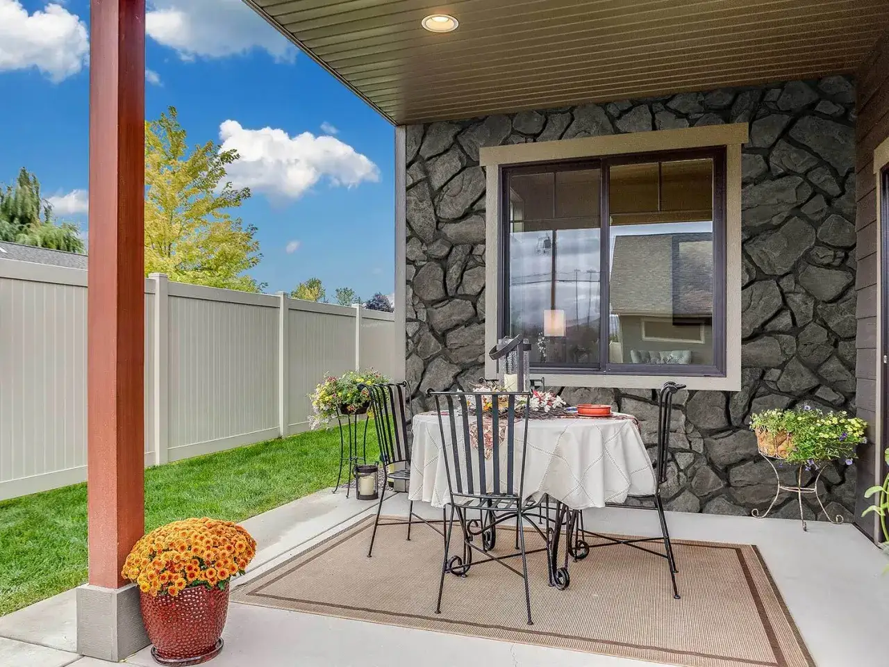 Acogedor patio con mesas y sillas, decorado con flores y un gran jarr&oacute;n de crisantemos. Las **patios con paredes de piedra** crean un ambiente r&uacute;stico y elegante.