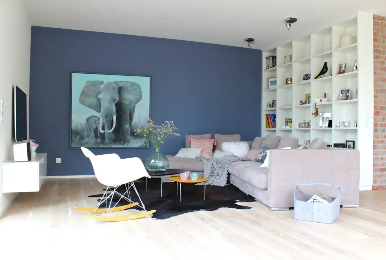 Ein Wohnzimmer mit einer tiefblauen Wand, die als Akzentfarbe dient. Ein großes Elefantenbild und ein weißer Schaukelstuhl stehen davor.