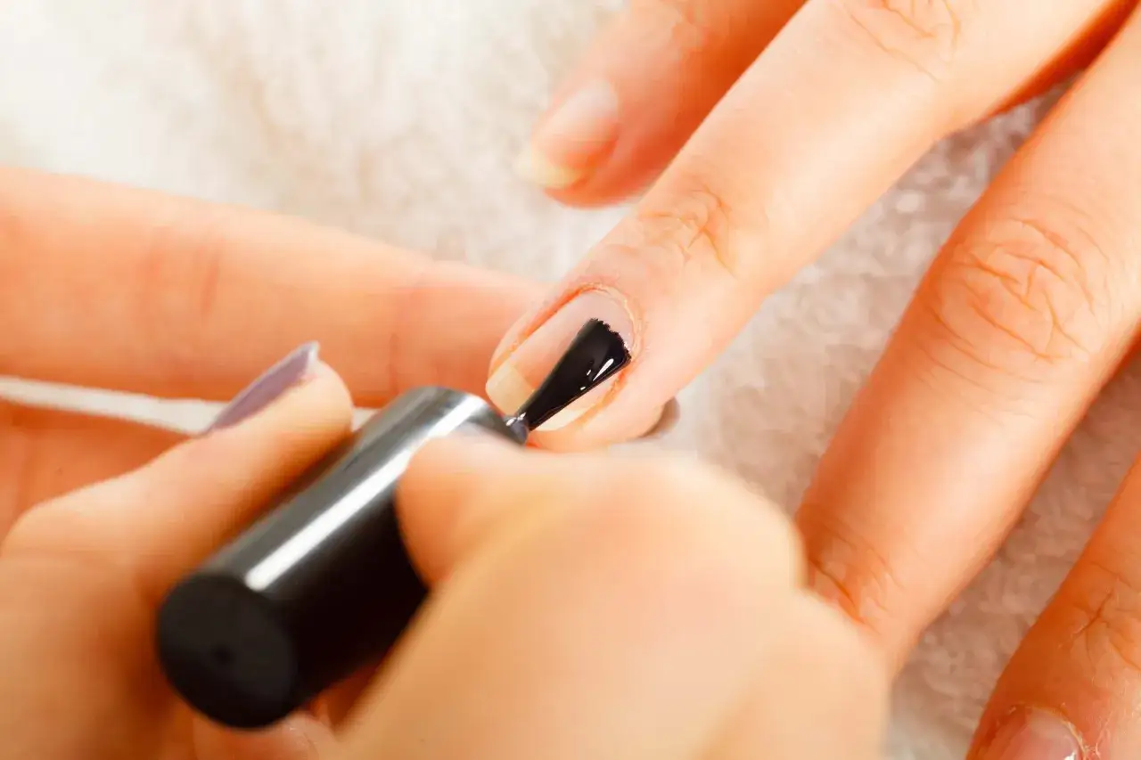 Application d'un vernis noir sur un ongle. Le top coat, c'est quoi ? C'est la touche finale pour prot&eacute;ger et faire briller.