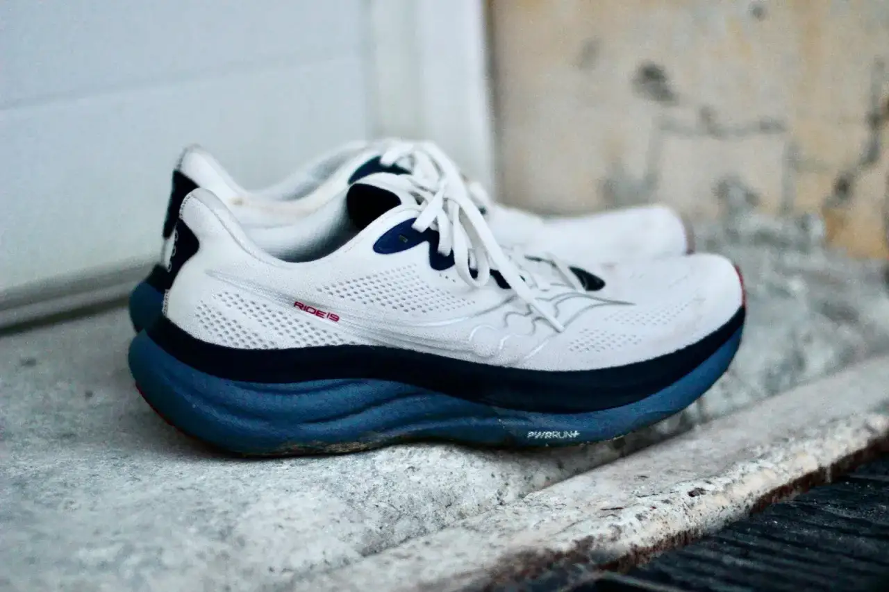 Weiße Laufschuhe, Saucony Ride 19, mit blauer Sohle und Schnürsenkeln, bereit für die nächste Laufrunde.