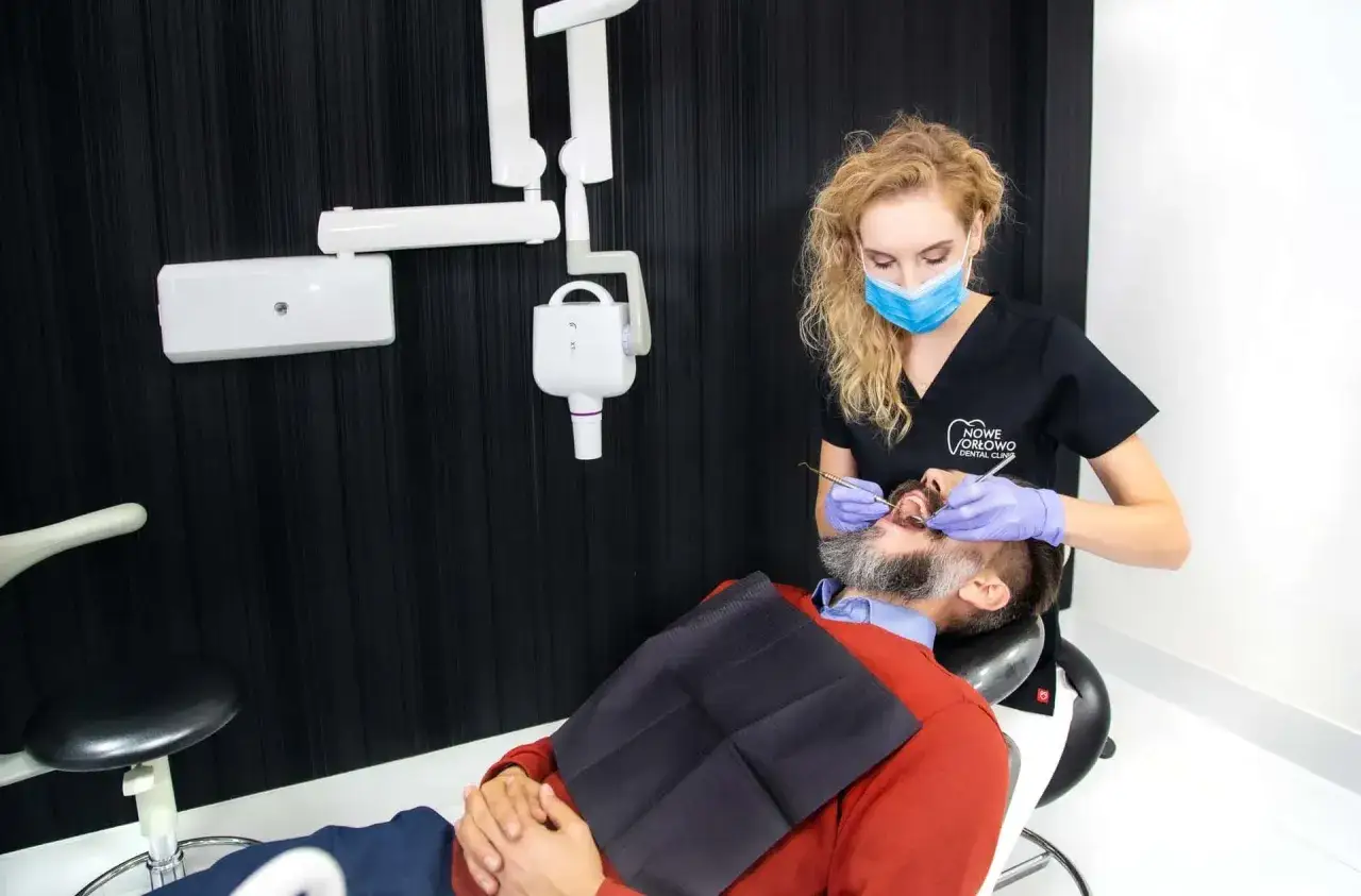 Dentystka bada zęby pacjenta, sprawdzając, czy nie ma ubytków klinowych.