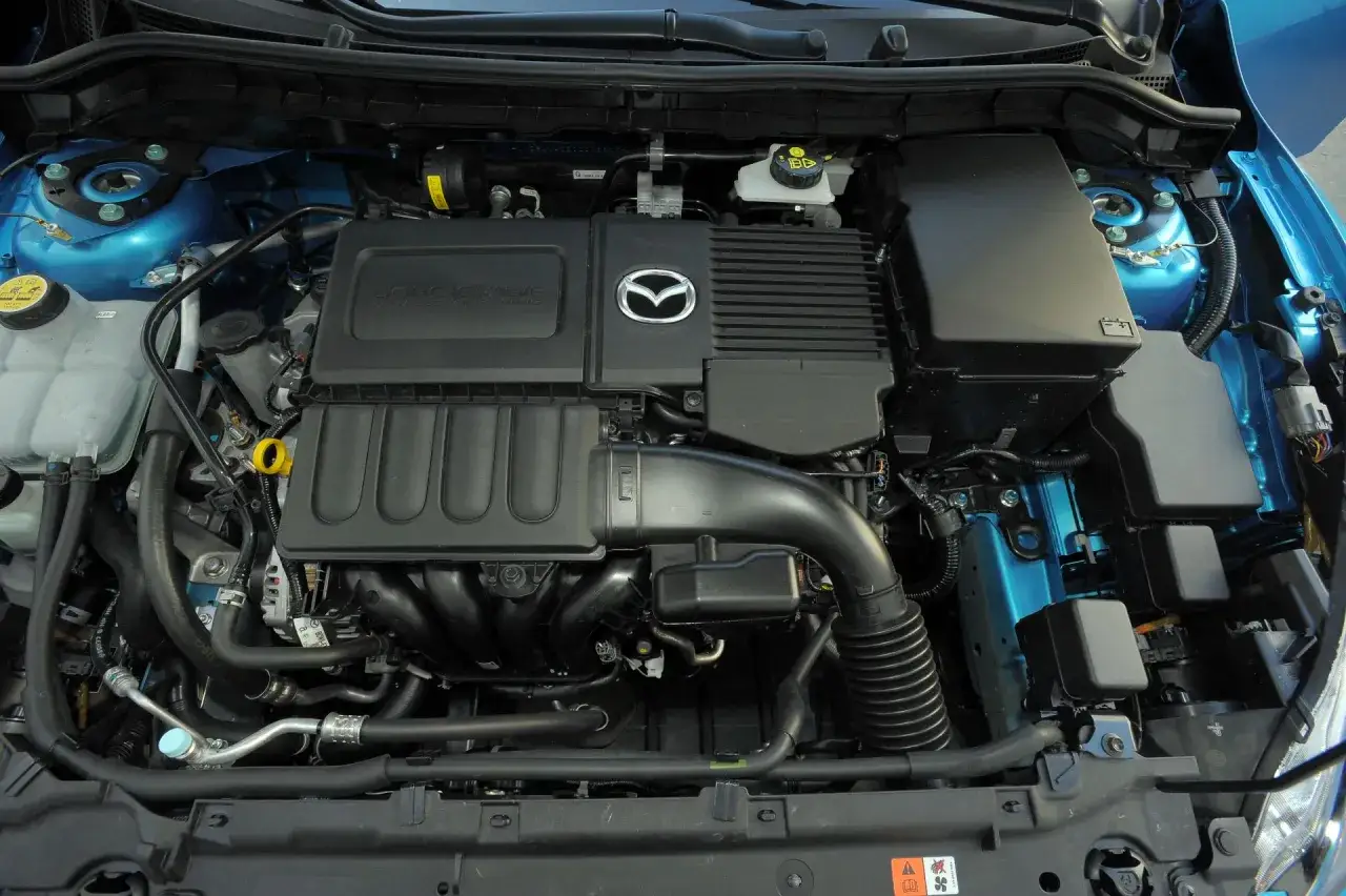 Silnik Mazdy 3 2010. Widoczny czarny kolektor dolotowy, pokrywa silnika z logo Mazdy i napisem DOHC 16 VALVE.