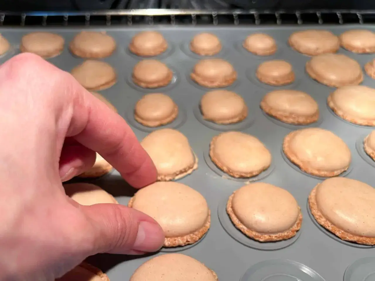 Eine Hand prüft die perfekt gebackenen Macarons auf einer Silikonmatte. Ein Schritt im Macarons Rezept.
