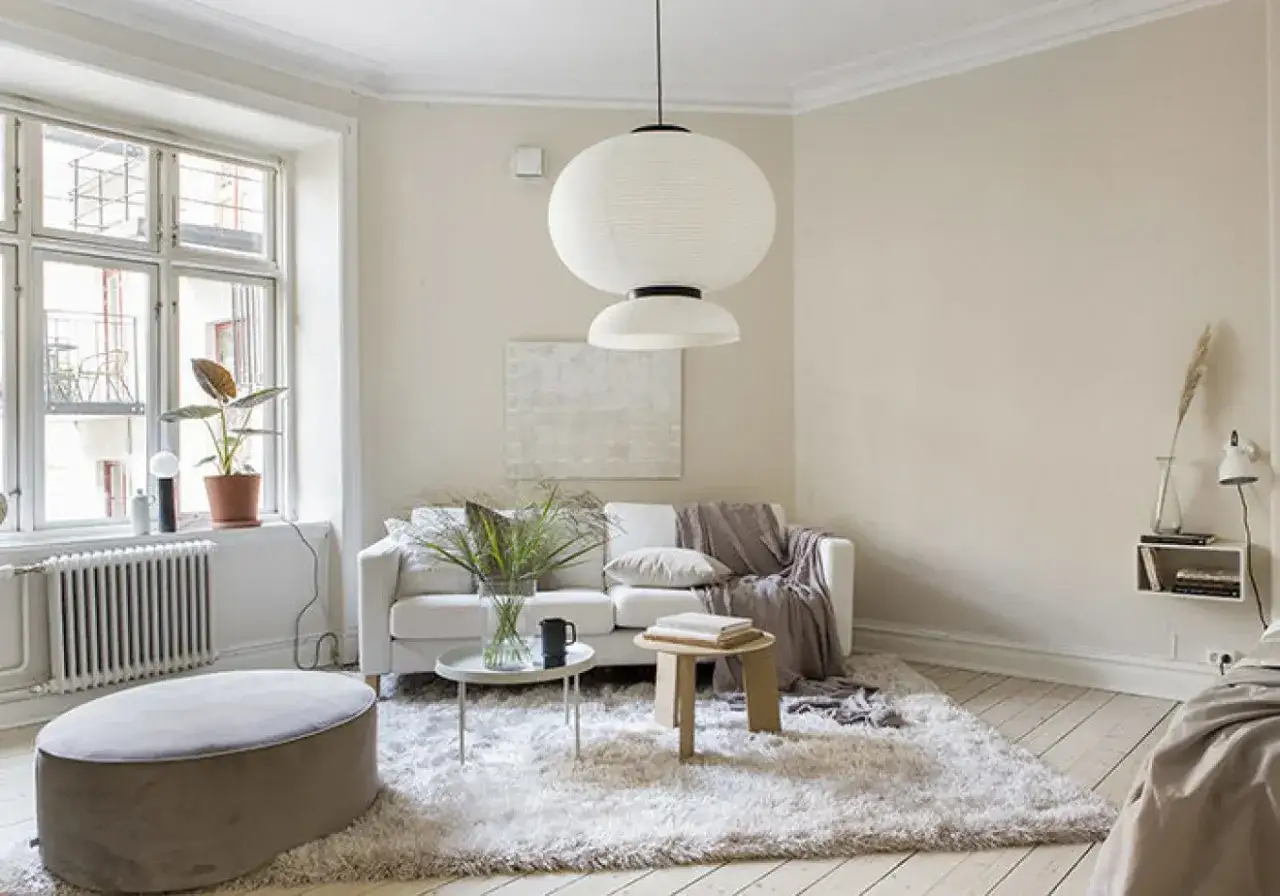 Ljust vardagsrum med en vit soffa, fluffig matta och en stor taklampa. Naturinredning med v&auml;xter och en avkopplande atmosf&auml;r.
