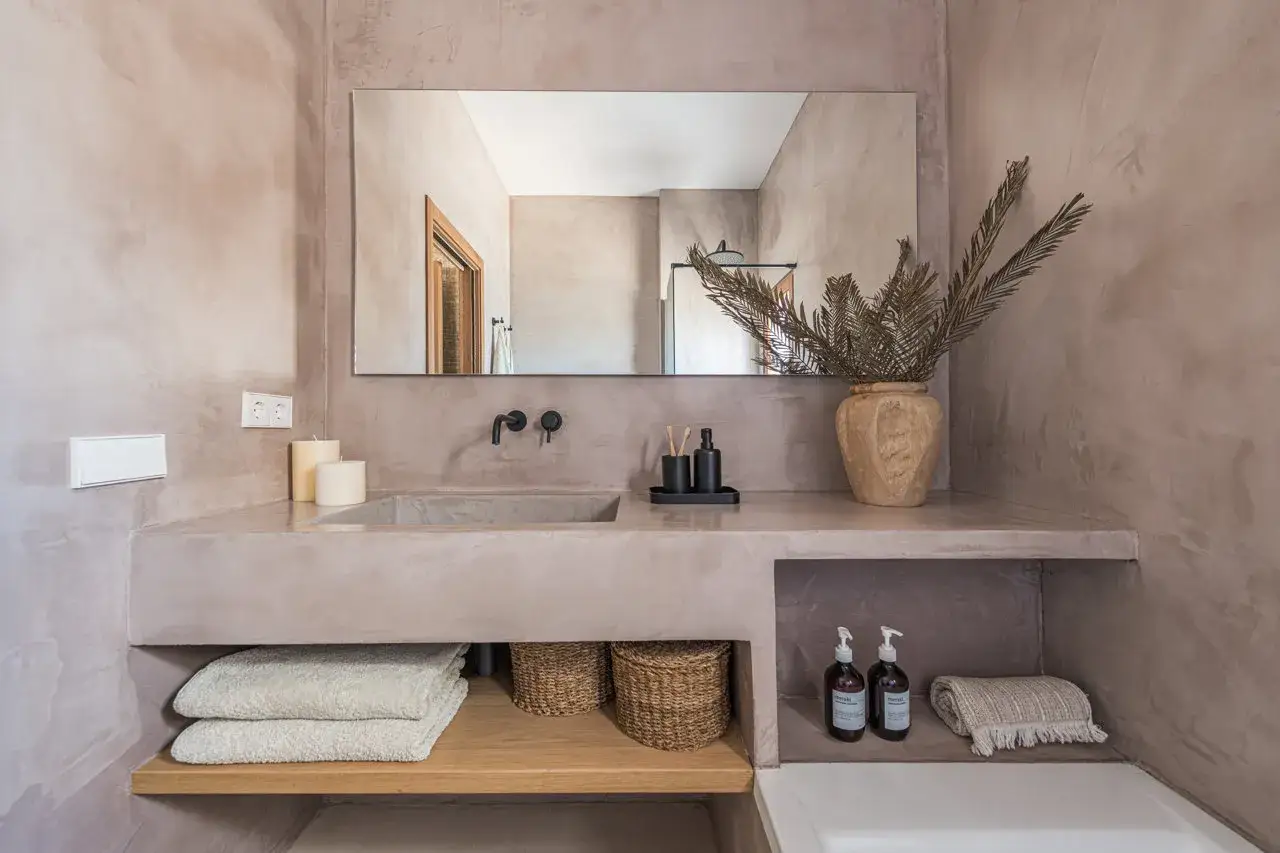 Lavabo de microcemento en ba&ntilde;o moderno, con espejo grande, toallas apiladas y decoraci&oacute;n natural.