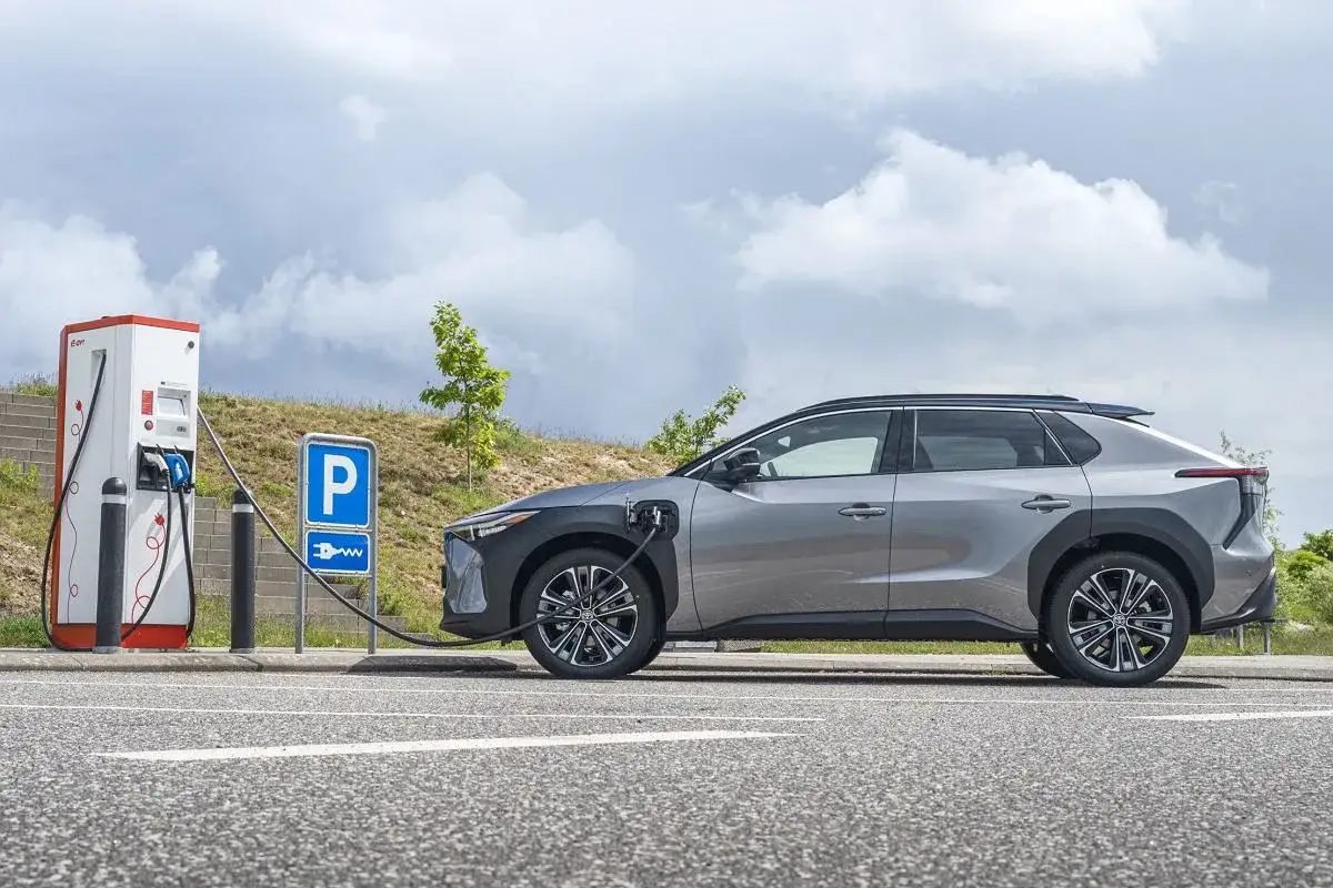 Srebrny Toyota bz4x ładuje się na stacji. Obok znak parkowania.