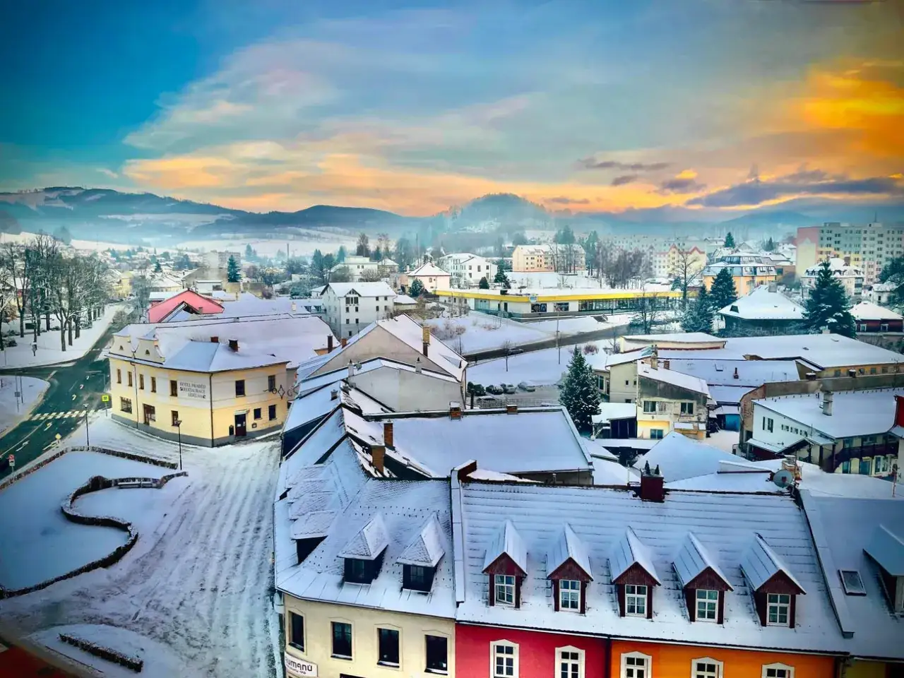 Zimowy krajobraz miasta w Czechach blisko granicy. Pokryte śniegiem dachy, górzyste tło i zachodzące słońce tworzą malowniczy widok.