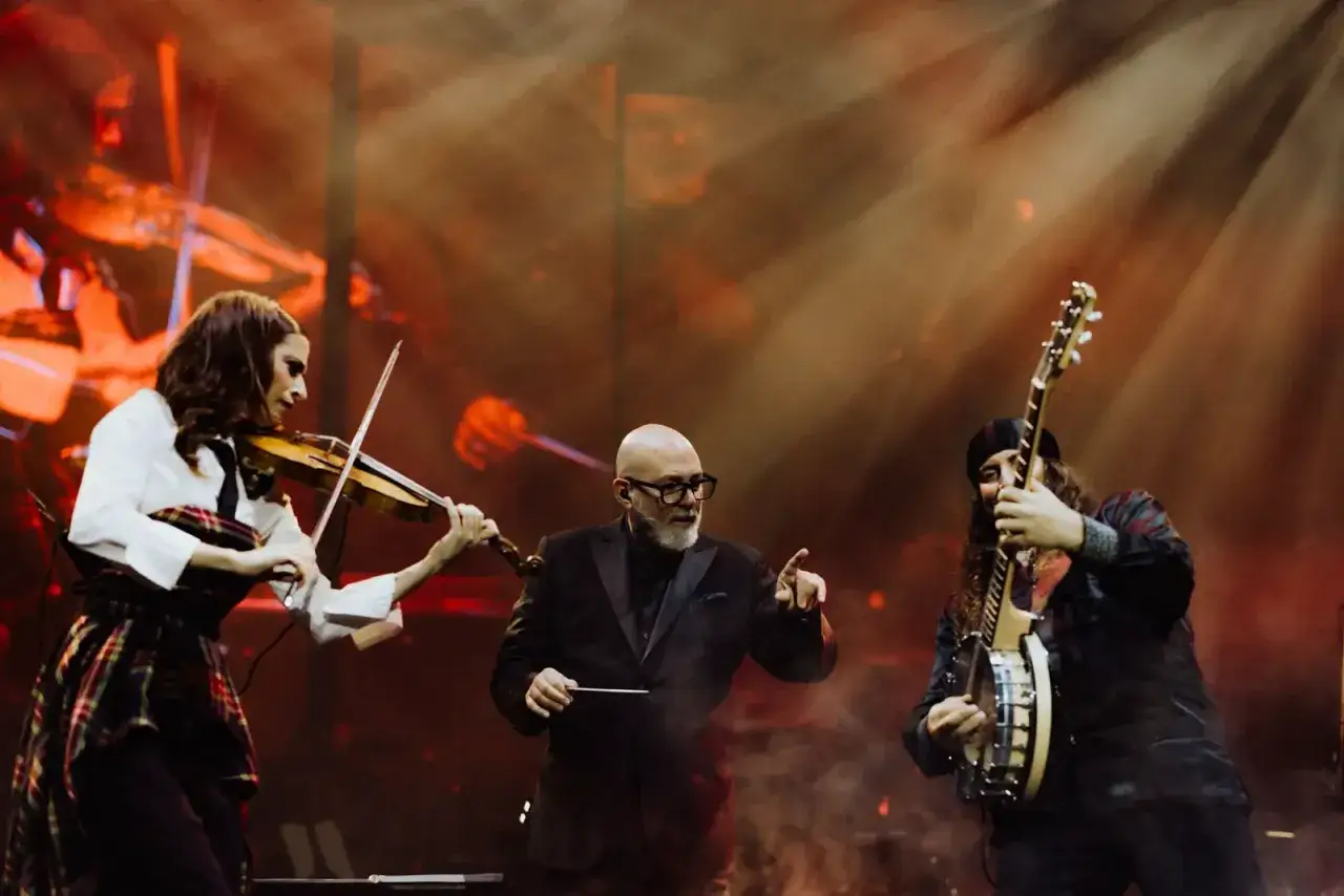 Ein Dirigent leitet ein Konzert mit Geige und Banjo. Die B&uuml;hne ist in warmes Licht getaucht, was an die Kunst von Hans Zimmer erinnert.