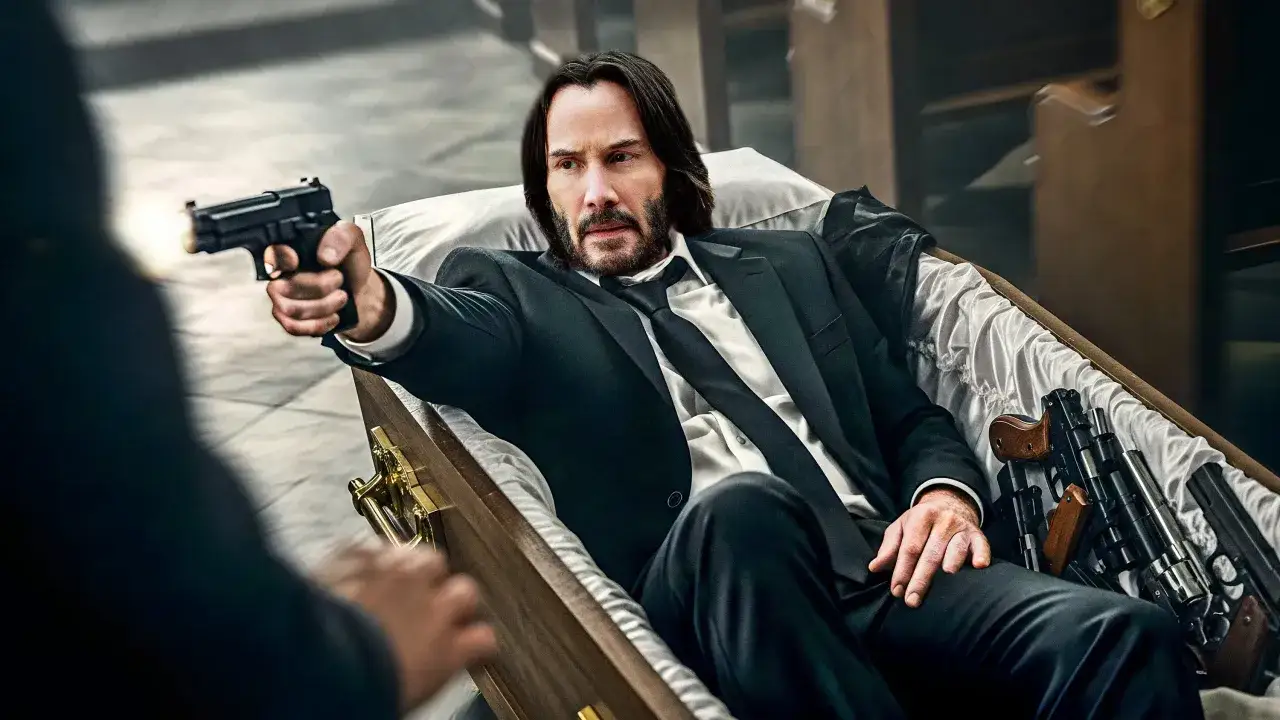 John Wick ligger i en kista, redo för John Wick 5, med vapen vid sin sida och en pistol i handen.