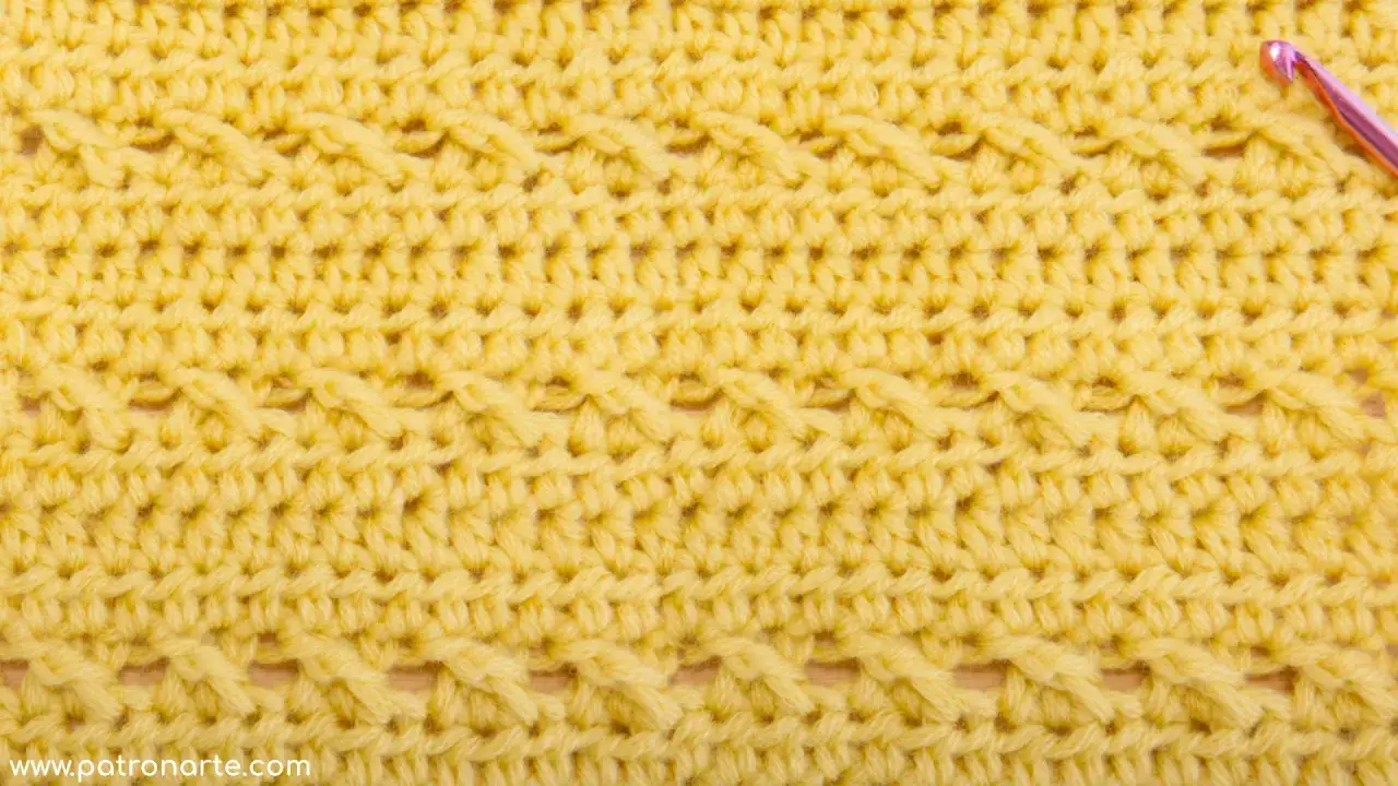 Textura de tejido cruzado en hilo amarillo, con un patr&oacute;n de trenzas y puntos que crean relieve.