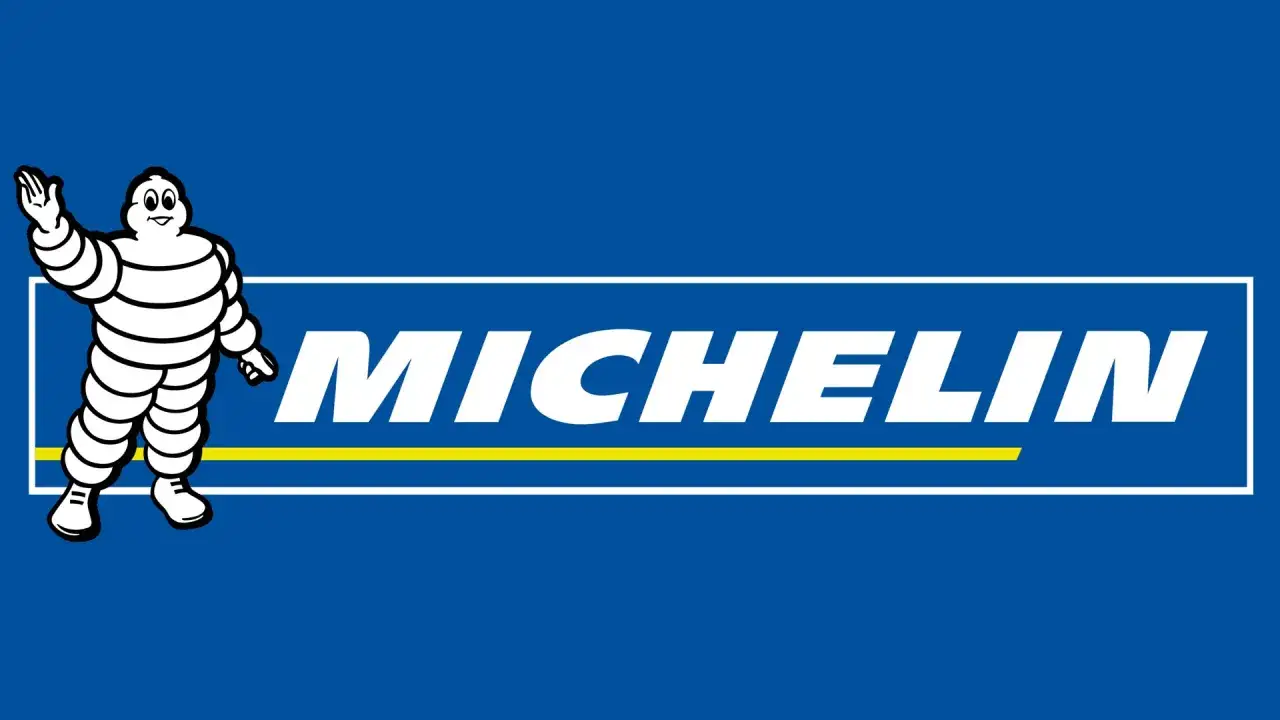 Bibendum, la mascotte de la sous marque Michelin, salue devant le logo blanc sur fond bleu.