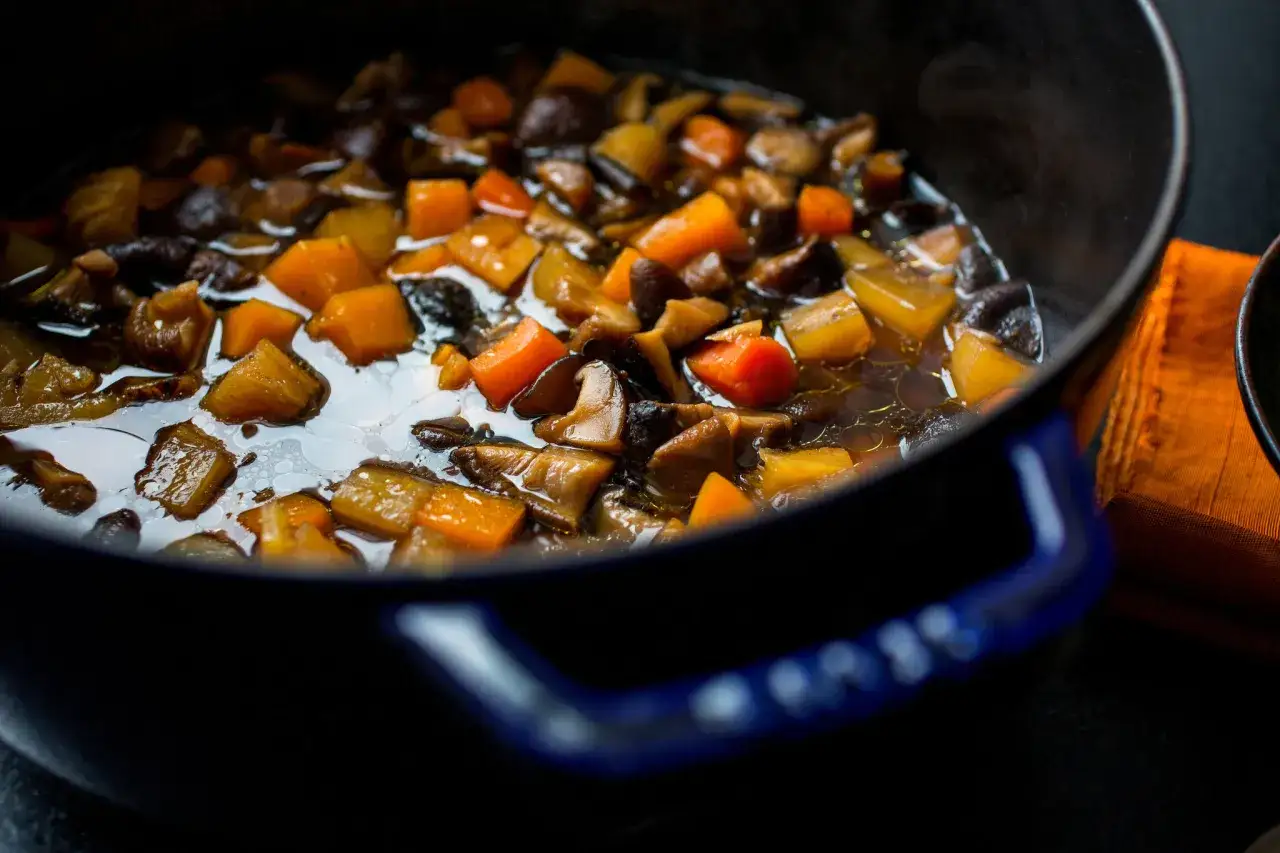 A close-up of a pot filled with simmering japanese root vegetables and mushrooms, ready to be served.