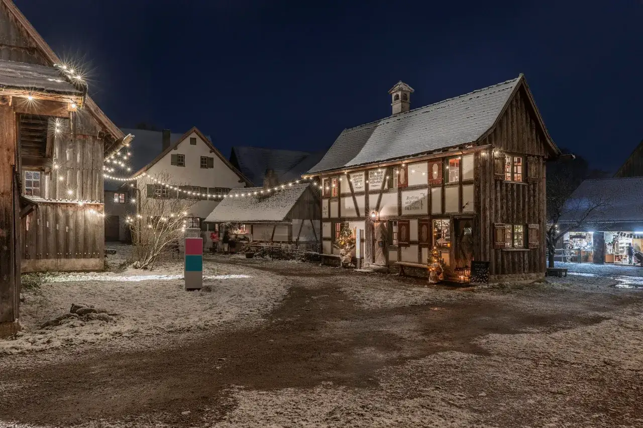 Winterliche Szene in einem Freilichtmuseum mit Fachwerkh&auml;usern, Lichterketten und Schnee. Hier wird gezeigt, was ein Freilichtmuseum ist.