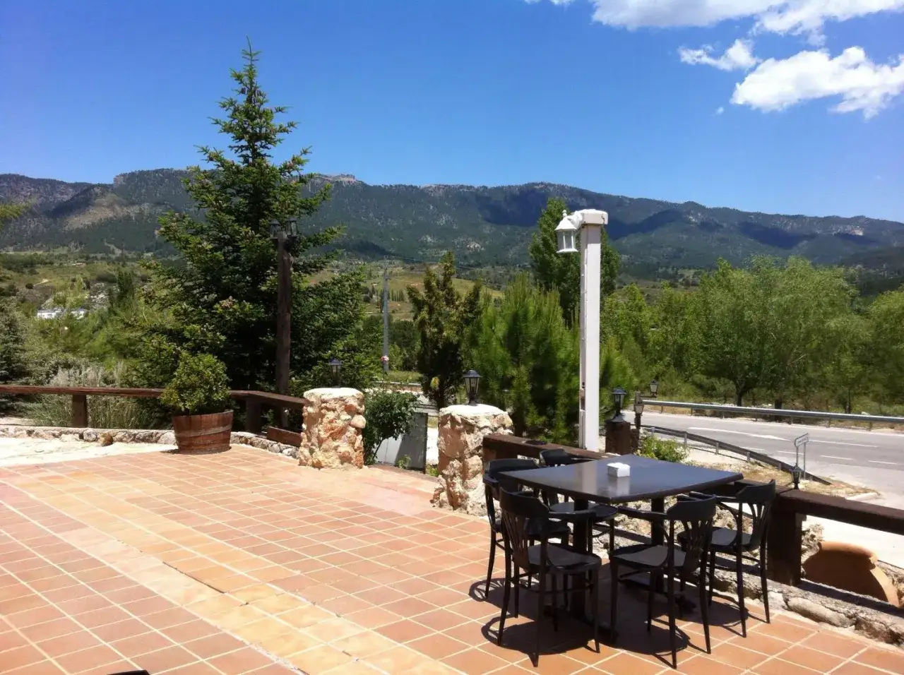 Terraza del restaurante El Gallego en Elche de la Sierra, con mesa y sillas, rodeada de pinos y montañas.
