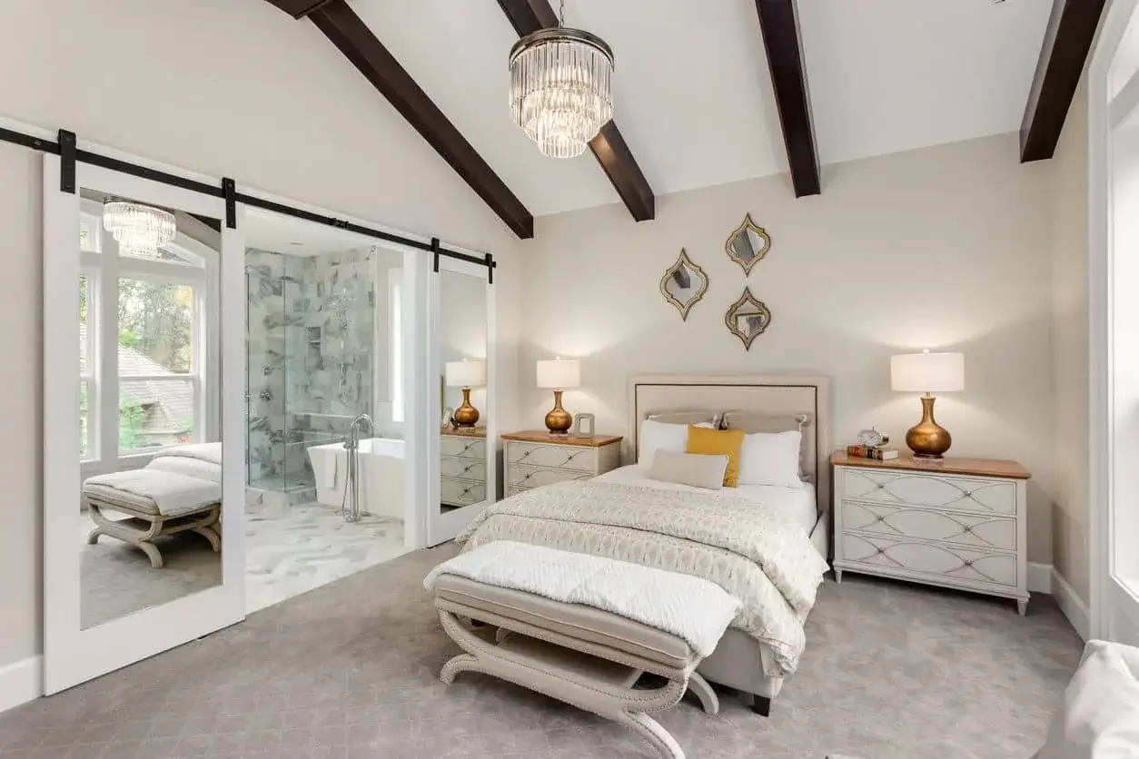 Ideas de iluminación para dormitorio de matrimonio: lámpara de araña, mesitas de noche con lámparas doradas y vigas oscuras en el techo.