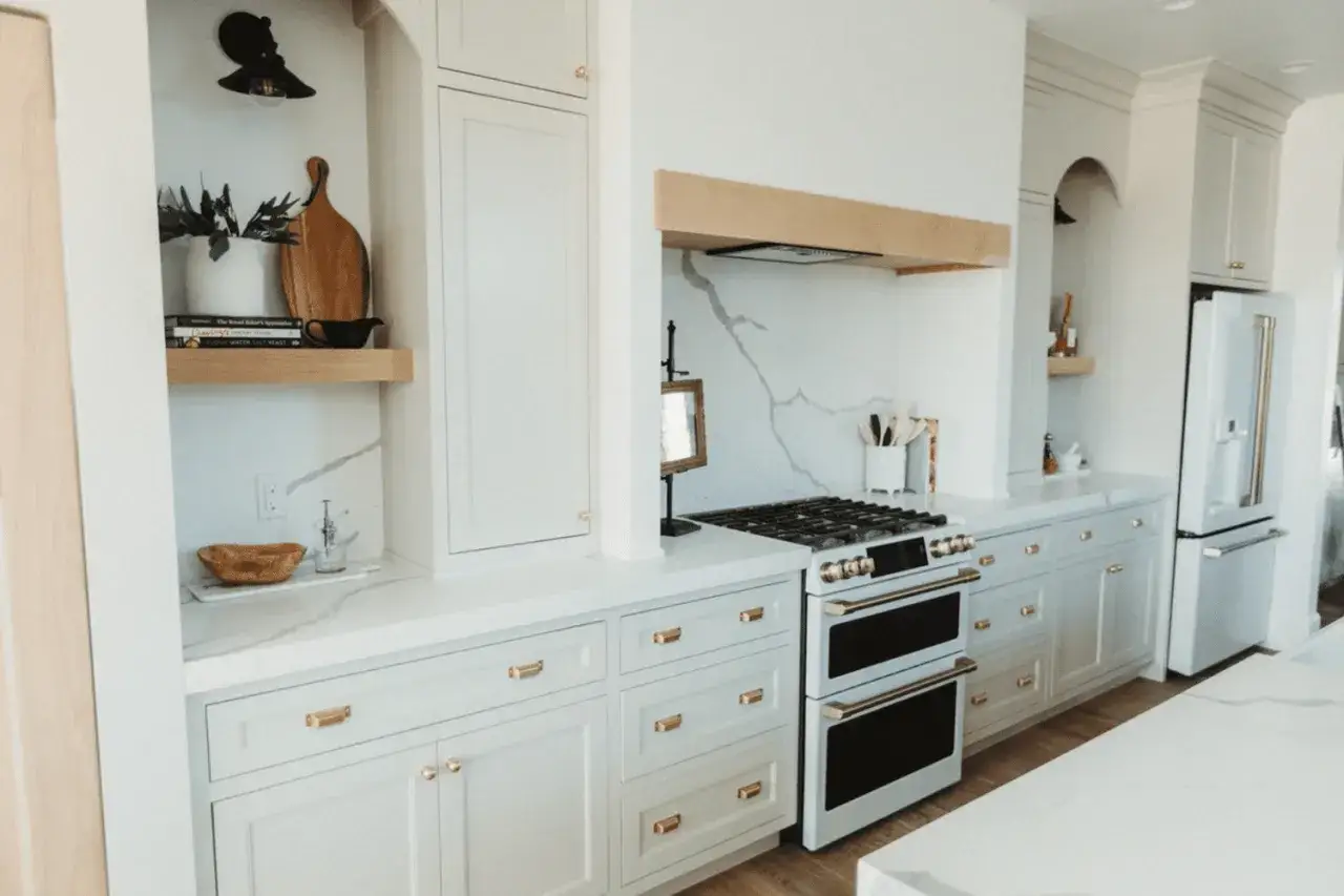 A bright, modern galley kitchen makeover featuring white cabinets, gold hardware, a marble backsplash, and a sleek gas range.