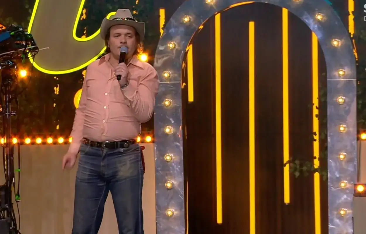 David Ritschard i cowboyhatt sjunger på Allsång på Skansen. Han bär en ljusrosa skjorta och jeans.