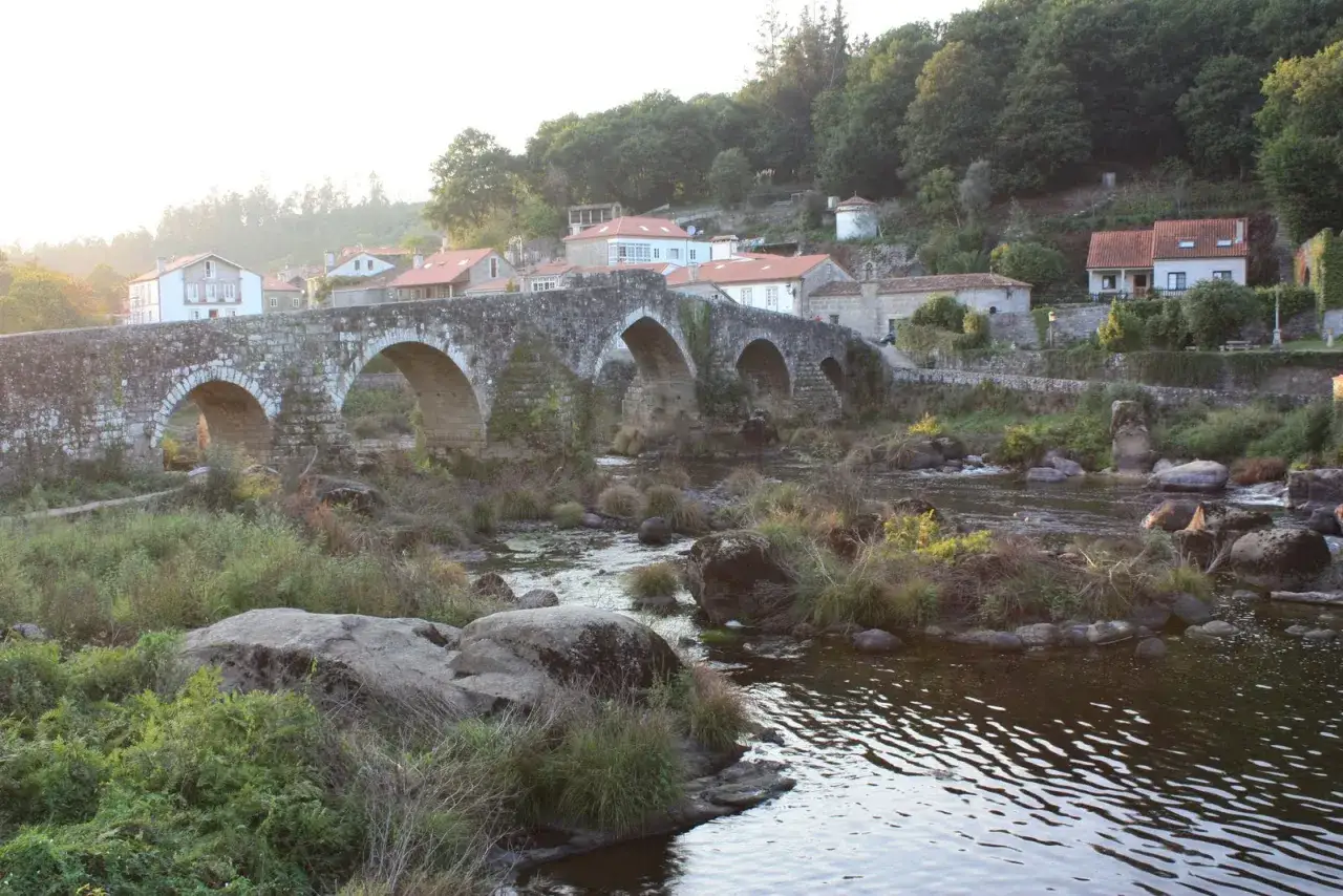 Ponte Maceira, un puente de piedra con arcos sobre un río, rodeado de casas y vegetación exuberante. ¡Qué bonito de ver!