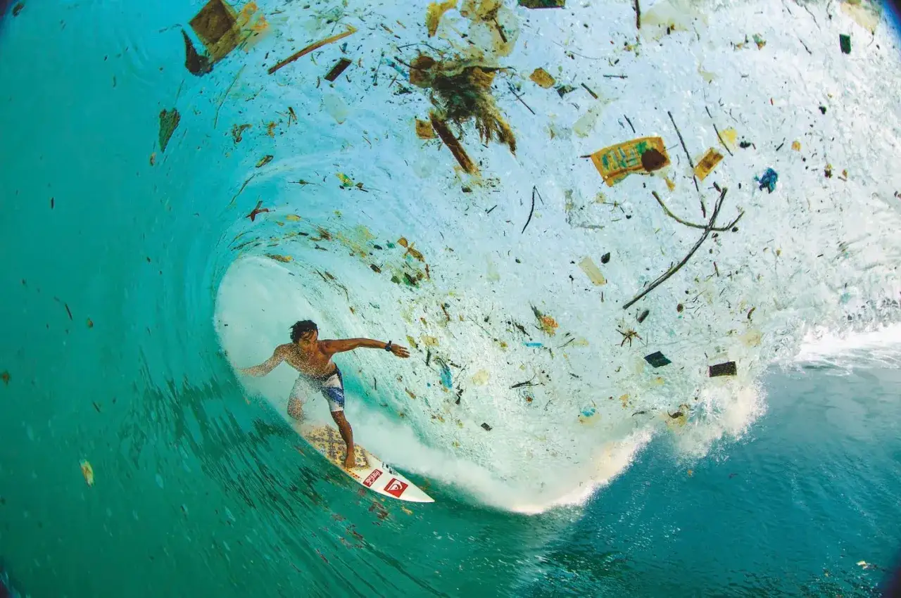 Surfer w tunelu zanieczyszczonej fali, otoczony śmieciami. Smutny widok tego, co znajduje się pod falą.