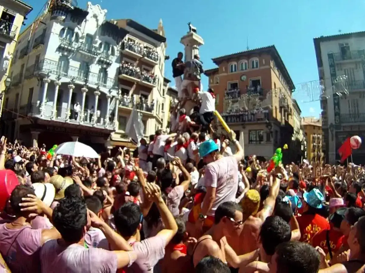 Multitud celebra el chupinazo de Teruel, con gente subida a un monumento y lanzando agua.