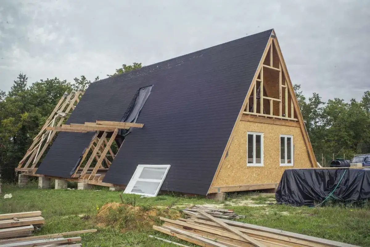 Maison en a prix, en pleine construction, avec sa toiture sombre et ses murs en bois. Des poutres et des fenêtres attendent d'être installées.