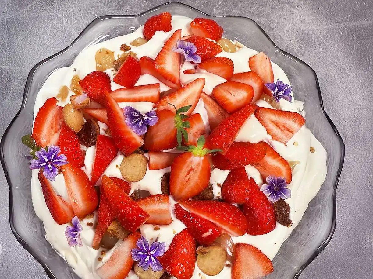 En härlig pavlova påskdessert med vispgrädde, färska jordgubbar och små lila blommor.