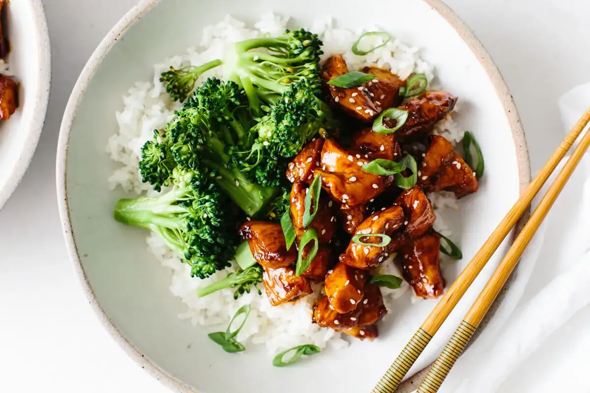 Schüssel mit Reis, gedünstetem Brokkoli und glasiertem Chicken Teriyaki, garniert mit Frühlingszwiebeln und Sesam.