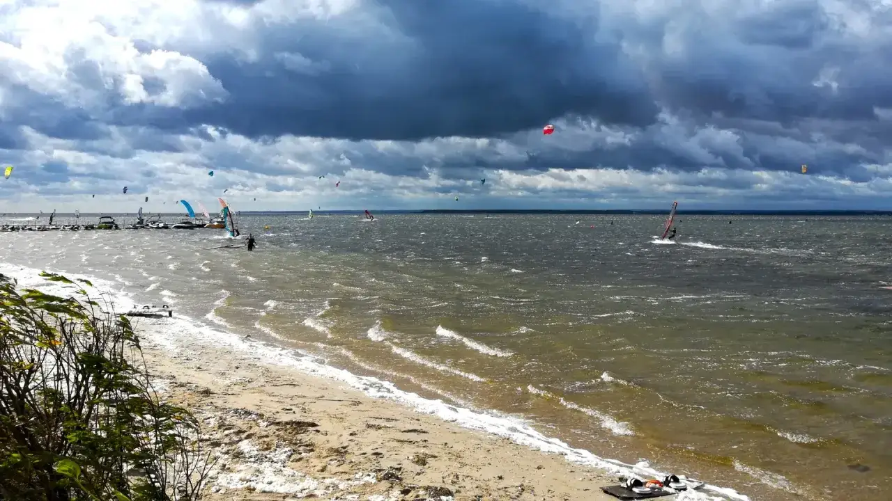 Wietrzny dzień sprzyja uprawianiu sportów wodnych. Na falach widać wielu surferów, którzy czerpią radość z **kite surfingu**.