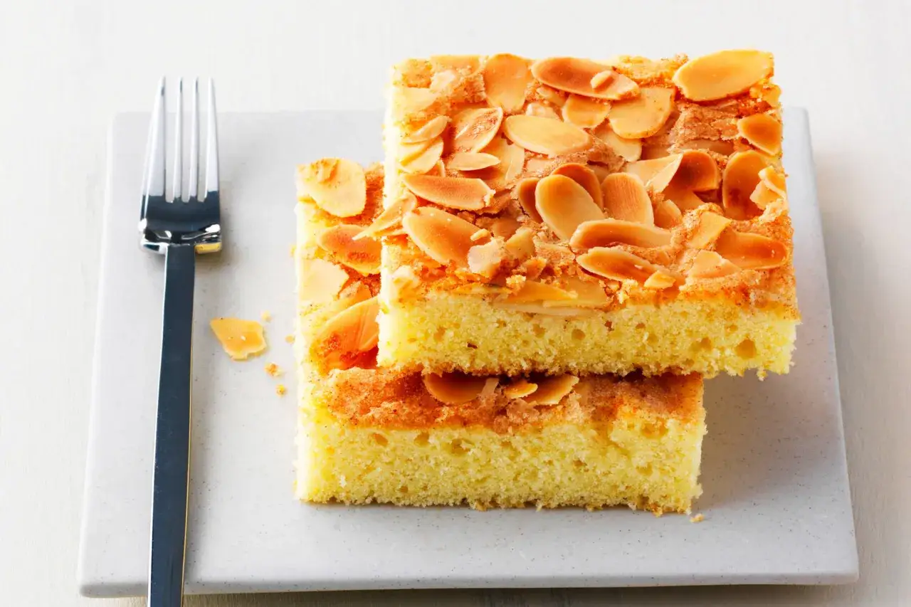 Zwei Stücke saftiger **Mandelkuchen vom Blech** mit knusprigen Mandelblättchen, bereit zum Genießen. Daneben eine Gabel.
