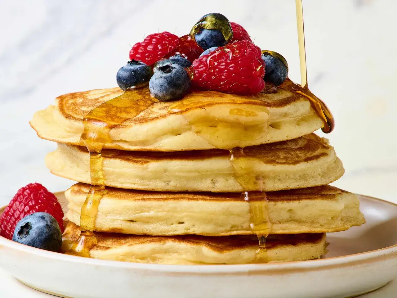 Ein Stapel fluffiger Pancakes, garniert mit Beeren und Sirup. Perfekt f&uuml;r ein gesundes Fr&uuml;hst&uuml;ck, wie dieses high protein pancakes rezept.