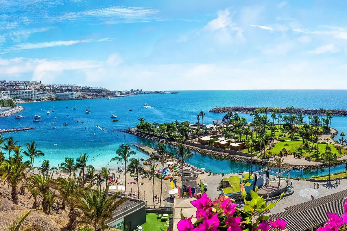 Słoneczna plaża, turkusowa woda i palmy – to typowe gran canaria atrakcje. Widok na zatokę z łodziami i kurortem.