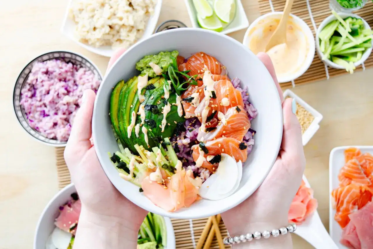 Frische Sushi Bowls mit Lachs, Avocado, Gurke und lila Reis, garniert mit Sesam und Nori.