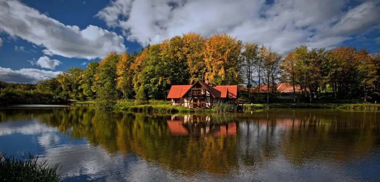 Malowniczy domek nad jeziorem, otoczony jesiennymi drzewami. Idealne miejsce, gdzie na weekend z dzieckiem jesienią.