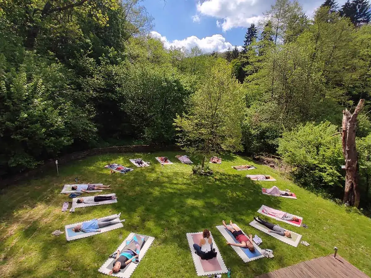 Yoga-Gruppe entspannt im Gr&uuml;nen. Menschen liegen auf Matten auf einer Wiese im Bergischen Land, umgeben von B&auml;umen.