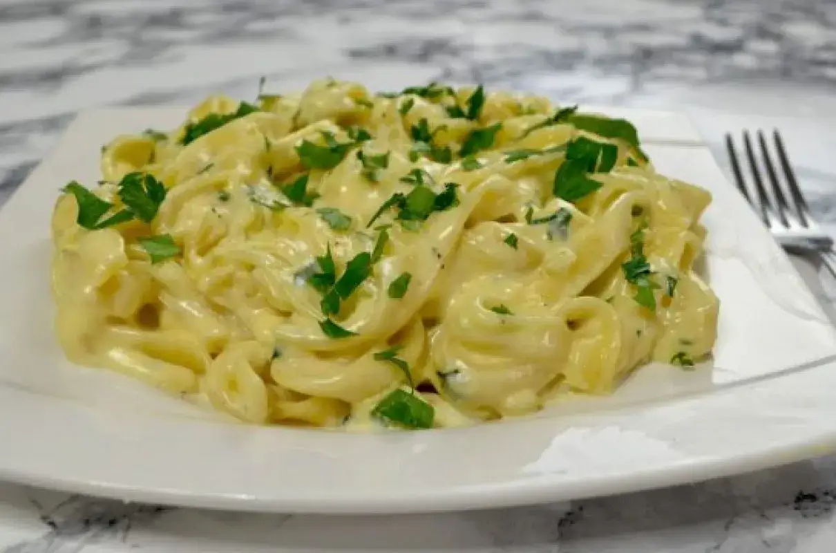 Pyszne, kremowe mac n cheese z posiekaną natką pietruszki, podane na białym talerzu.