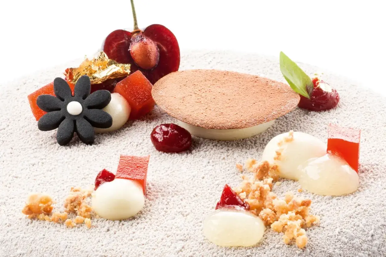 Délicieux dessert avec des fruits rouges, des cubes de gelée rouge et des sphères crémeuses, le tout saupoudré de cacao.