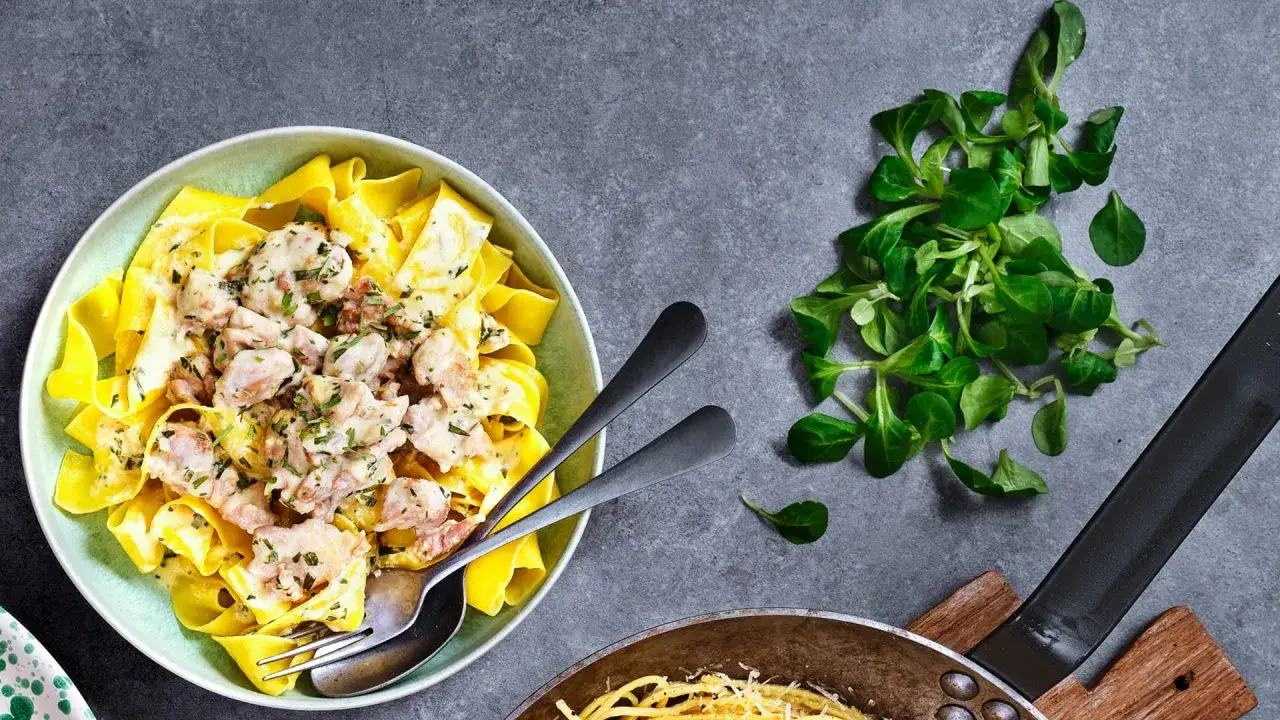 En krämig pasta med kyckling, som en riktig dragon kyckling i ugn, serveras i en ljusgrön skål. Bredvid ligger en hög med färsk sallat.