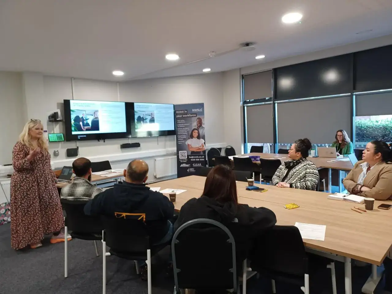 A trainer leads a management and leadership training session for a diverse group of professionals in a modern classroom.