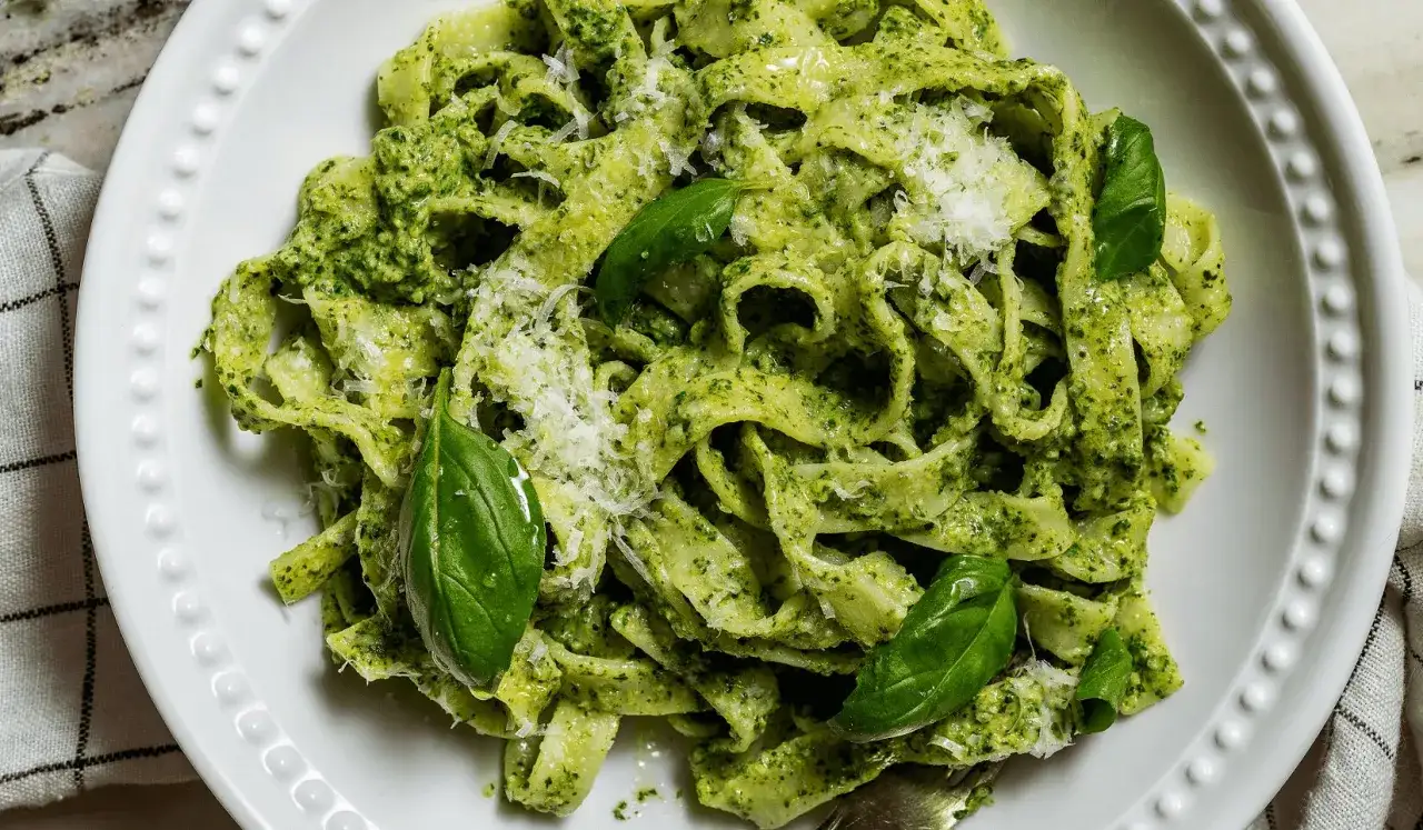 Pasta fresca con salsa de espinacas y albahaca, espolvoreada con queso parmesano rallado y decorada con hojas de albahaca fresca.