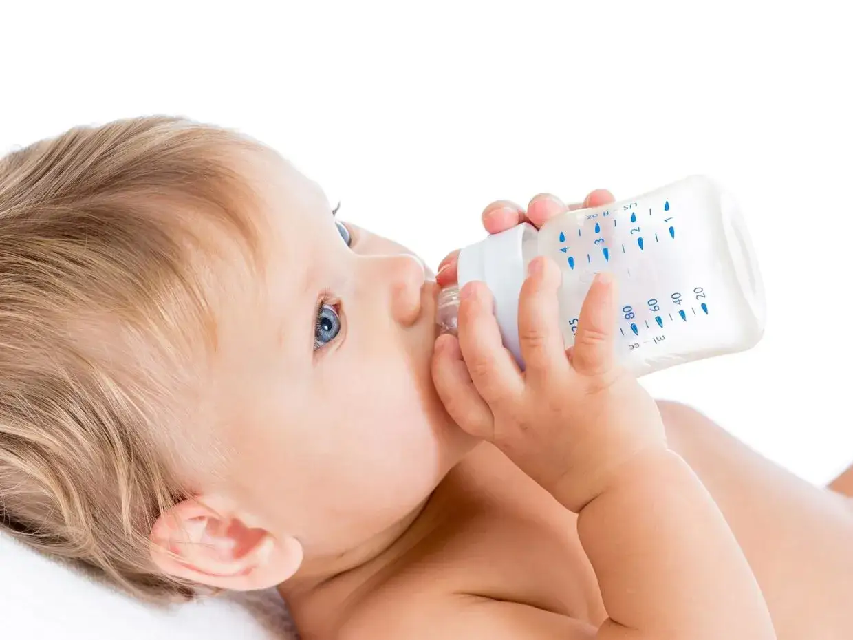 Bambino con occhi azzurri beve dal biberon, sperando che aiuti con la stitichezza neonato.