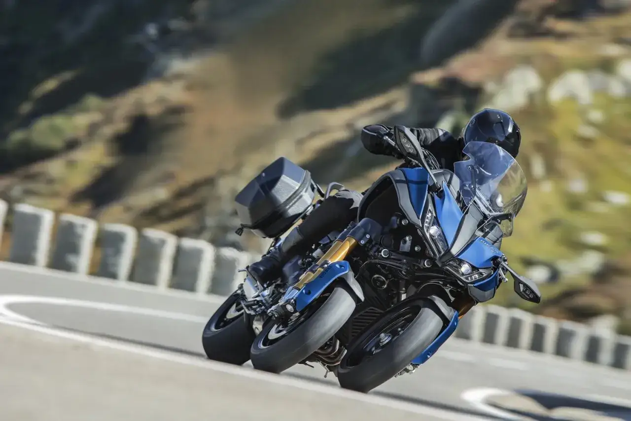 Motocyklista na niebieskim Yamaha Niken pochyla się na zakręcie górskiej drogi, ciesząc się jazdą.