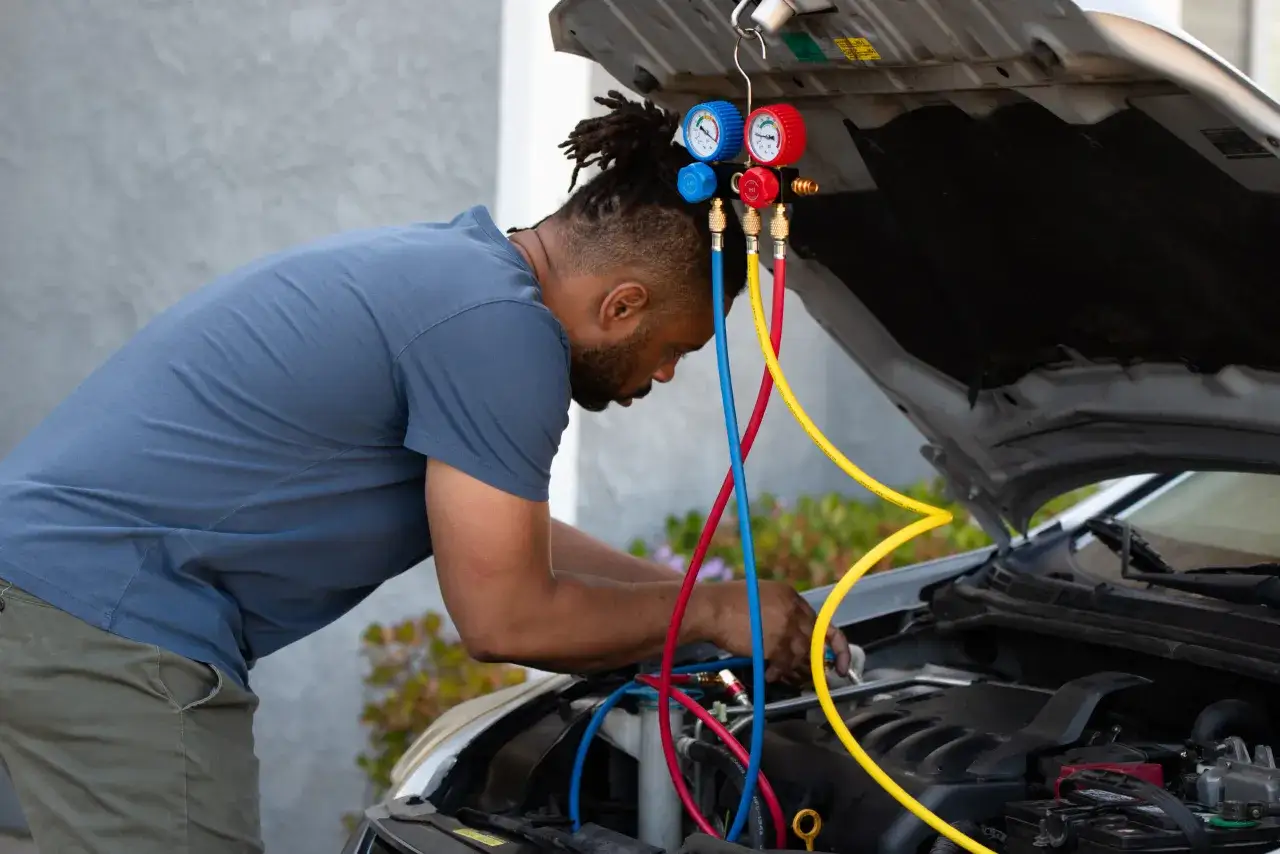 Mekaniker kontrollerar bilens AC-system med m&auml;tare och slangar. F&ouml;rhoppningsvis l&ouml;ser det problemet att bilen bl&aring;ser bara kall luft.
