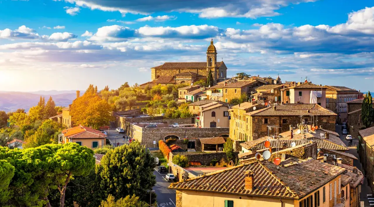 Sonnenuntergang &uuml;ber Montalcino, Toskana. Malerische H&uuml;gelstadt mit mittelalterlicher Architektur und Kirchturm, umgeben von gr&uuml;nen H&uuml;geln.