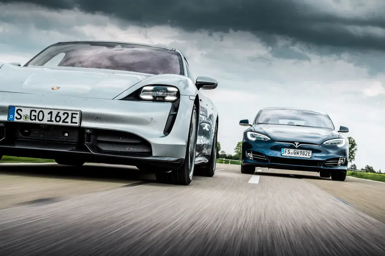 Srebrny porsche elektryczne i niebieski Tesla jadą obok siebie po drodze.
