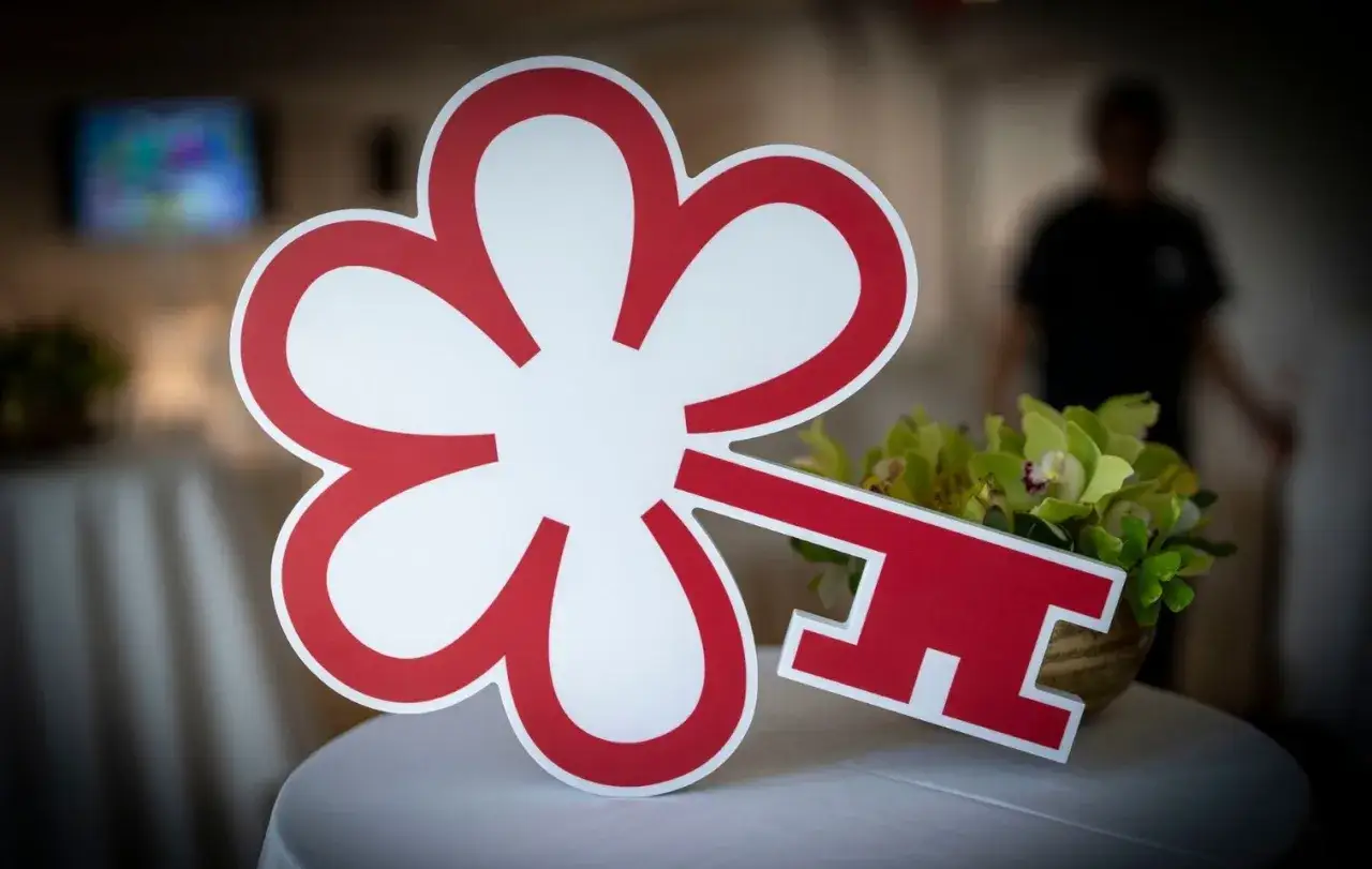 Chiave rossa a forma di fiore, simbolo della Guida Michelin, appoggiata su un tavolo con fiori verdi.