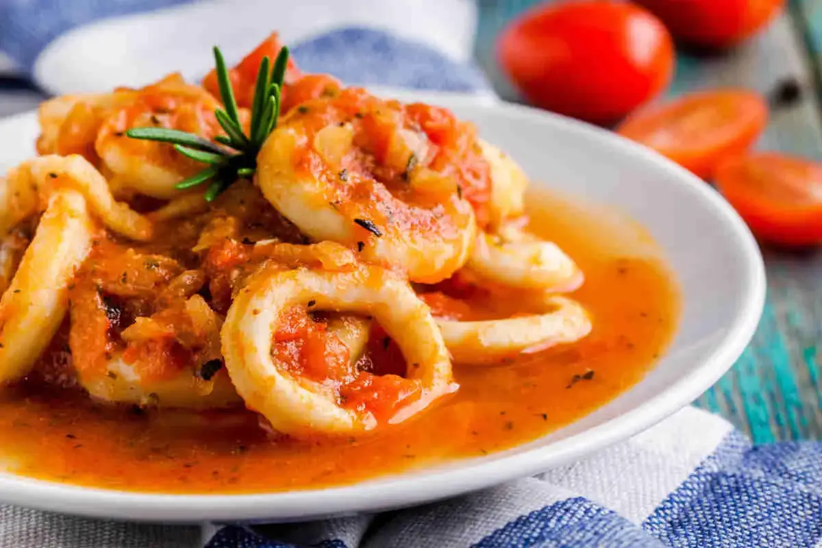 Anelli di totani in umido, un piatto saporito con pomodoro e rosmarino, servito su un piatto bianco.