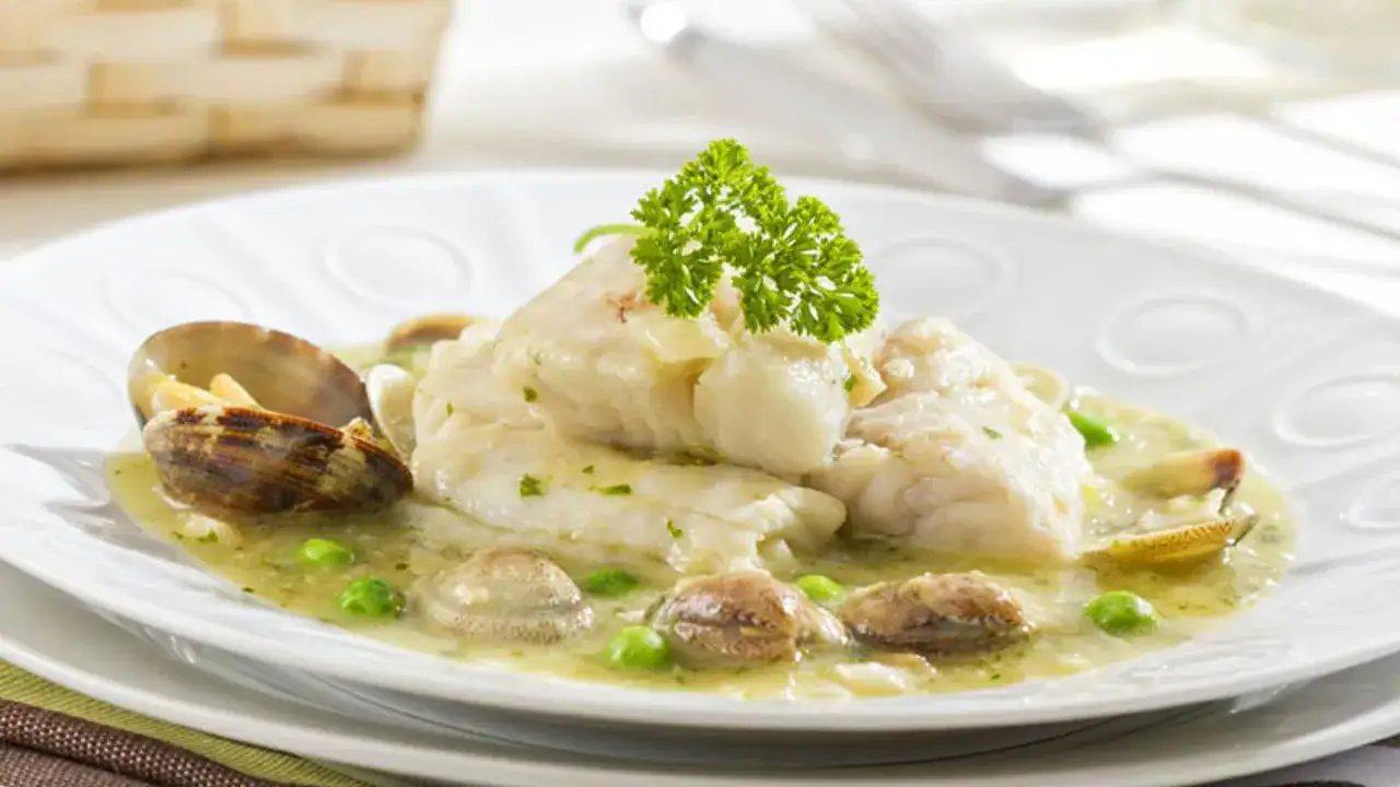 Merluza en salsa verde con almejas y guisantes, decorada con perejil fresco. Un plato marinero delicioso.