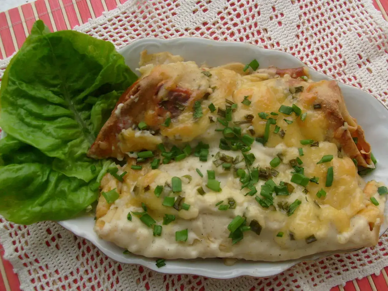 Zapiekane naleśniki z mięsem, polane sosem i posypane szczypiorkiem, obok liść sałaty. Danie wygląda jak cannoloni kontra naleśniki z mięsem.