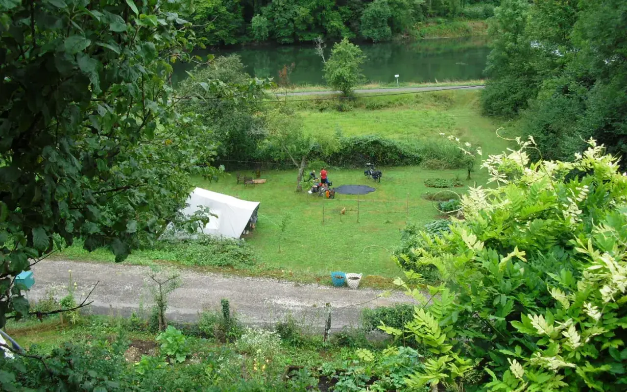 Un campement paisible pour un camping chez l'habitant en France, avec une tente blanche, des vélos et un plan d'eau verdoyant en arrière-plan.